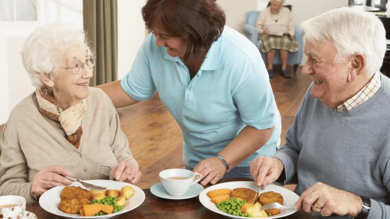 A caregiver serves a nutritious meal to seniors, promoting healthy holiday eating habits.