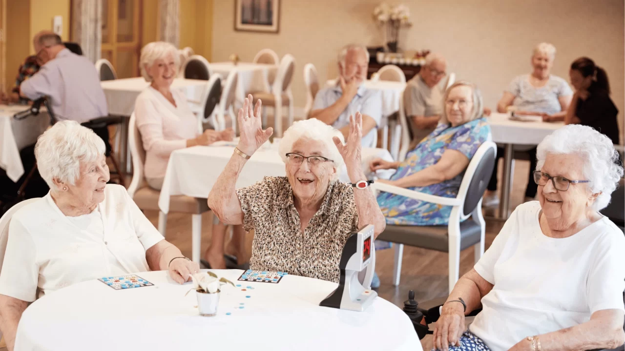 Elderly individuals enjoying activities together at tables in an assisted living facility.